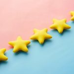 Yellow stars on pink and blue pastel background for rating or review concept.